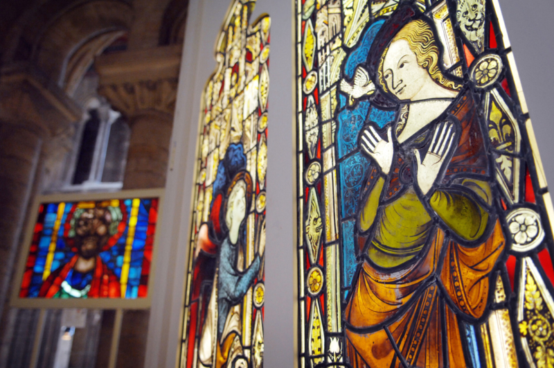 Close-up view of a stain glass window of a lady with blonde hair and a bird flying over to her inside of a church.